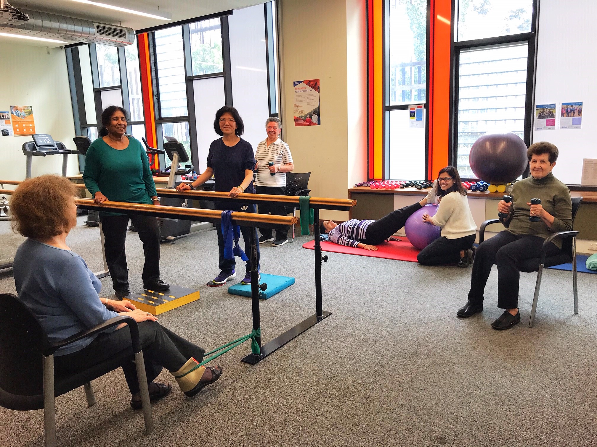 A group of women exercise in a room together, smiling at the camera.